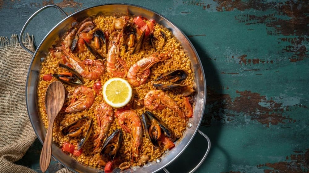 Seafood paella in a traditional pan, garnished with shrimp, mussels, and lemon wedges, served at a beachside restaurant in Valencia, Spain.