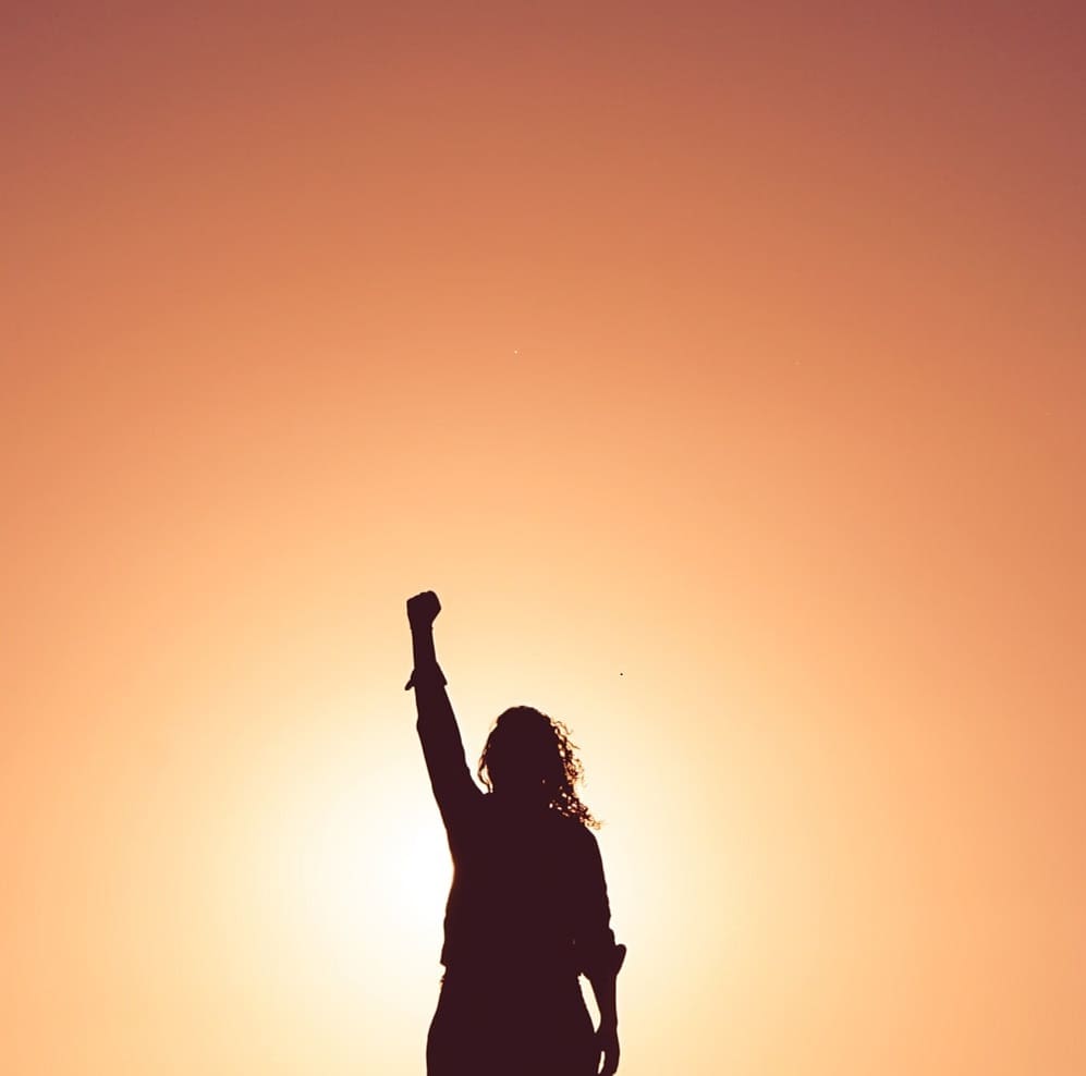 A girl wih her right arm up in front of the sun