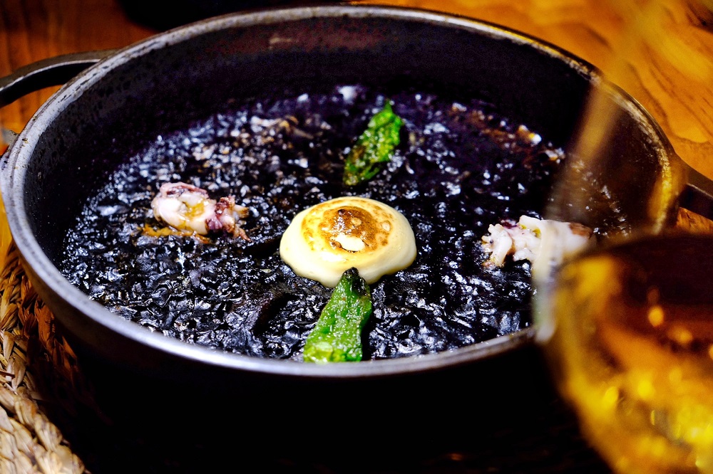 A cook cooking a tasty arroz negro dish, that is another paella version.