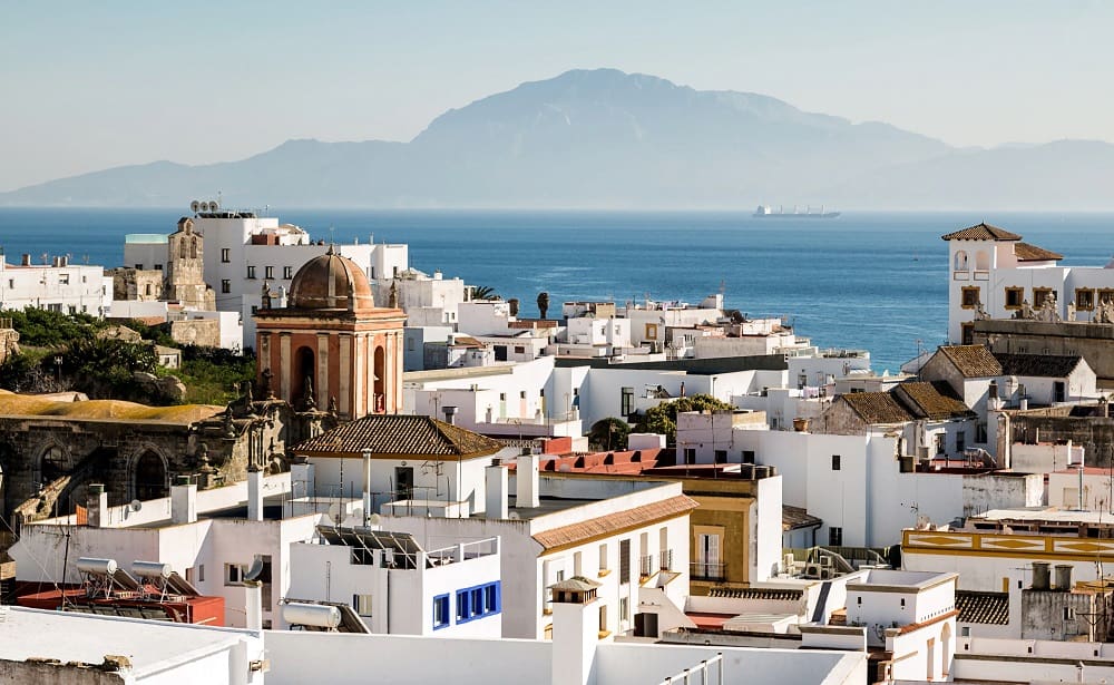 Panoramic view of Cádiz's skyline with its iconic cathedral, ancient buildings, and the shimmering Atlantic Ocean in the backdrop.