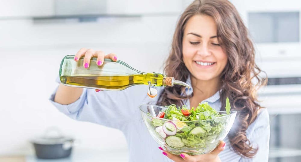 A woman drizzling Spanish olive oil over a fresh salad, highlighting the use of olive oil in daily cooking.