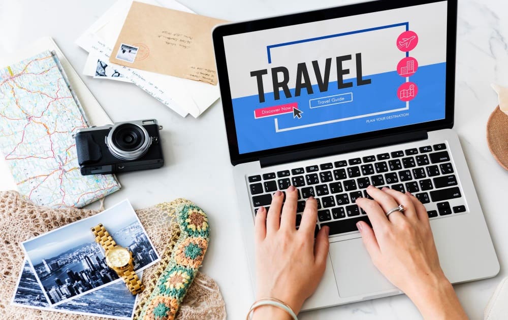 A laptop with the word 'Travel' on the screen, surrounded by travel essentials like a map, compass, and camera, symbolizing the process of planning a trip